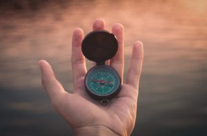hand holding a compass against a vague brown background