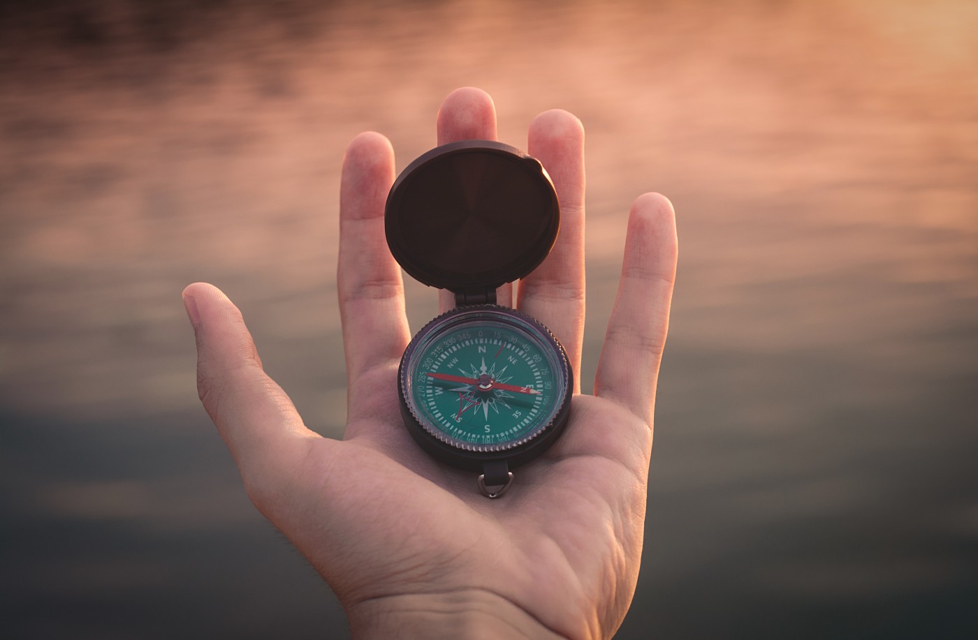 hand holding a compass against a vague brown background