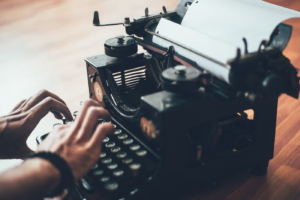 hands on an old typewriter on a wooden desk