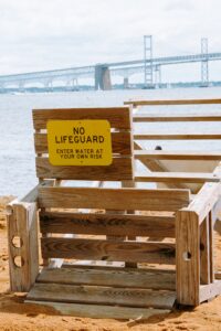 toppled life guard stand on a beach with a massive suspension bridge in the background and a sign that says 'no lifeguard'