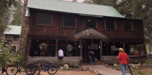 an old two story mountain lodge of stone and logs with people and bicycles hanging out upfront - deep appreciation for Earth