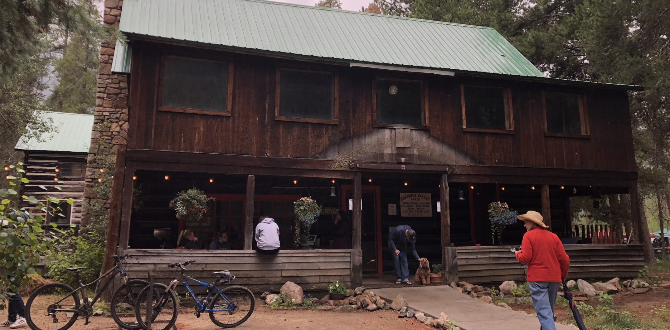 an old two story mountain lodge of stone and logs with people and bicycles hanging out upfront - deep appreciation for Earth