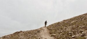 a single woman hiking in the distance on a treeless trail against a gray sky