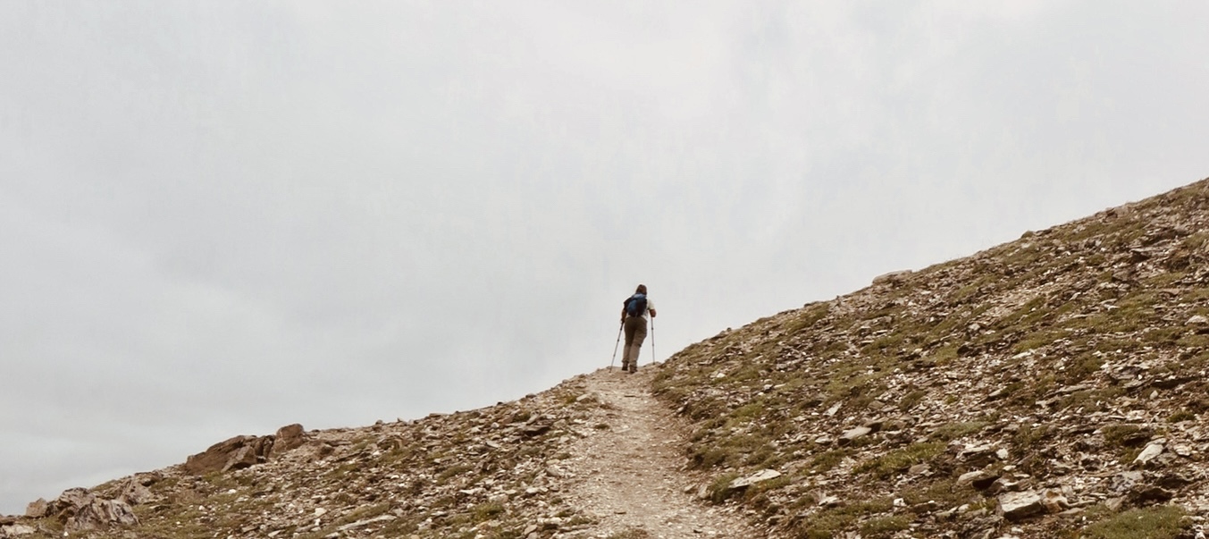 a single woman hiking in the distance on a treeless trail against a gray sky